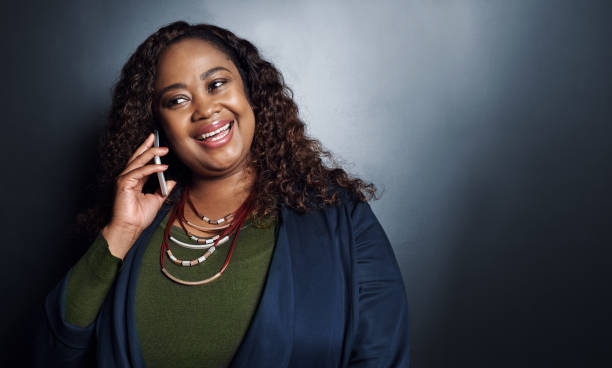 Cropped shot of an attractive young businesswoman making a call while standing against a dark background